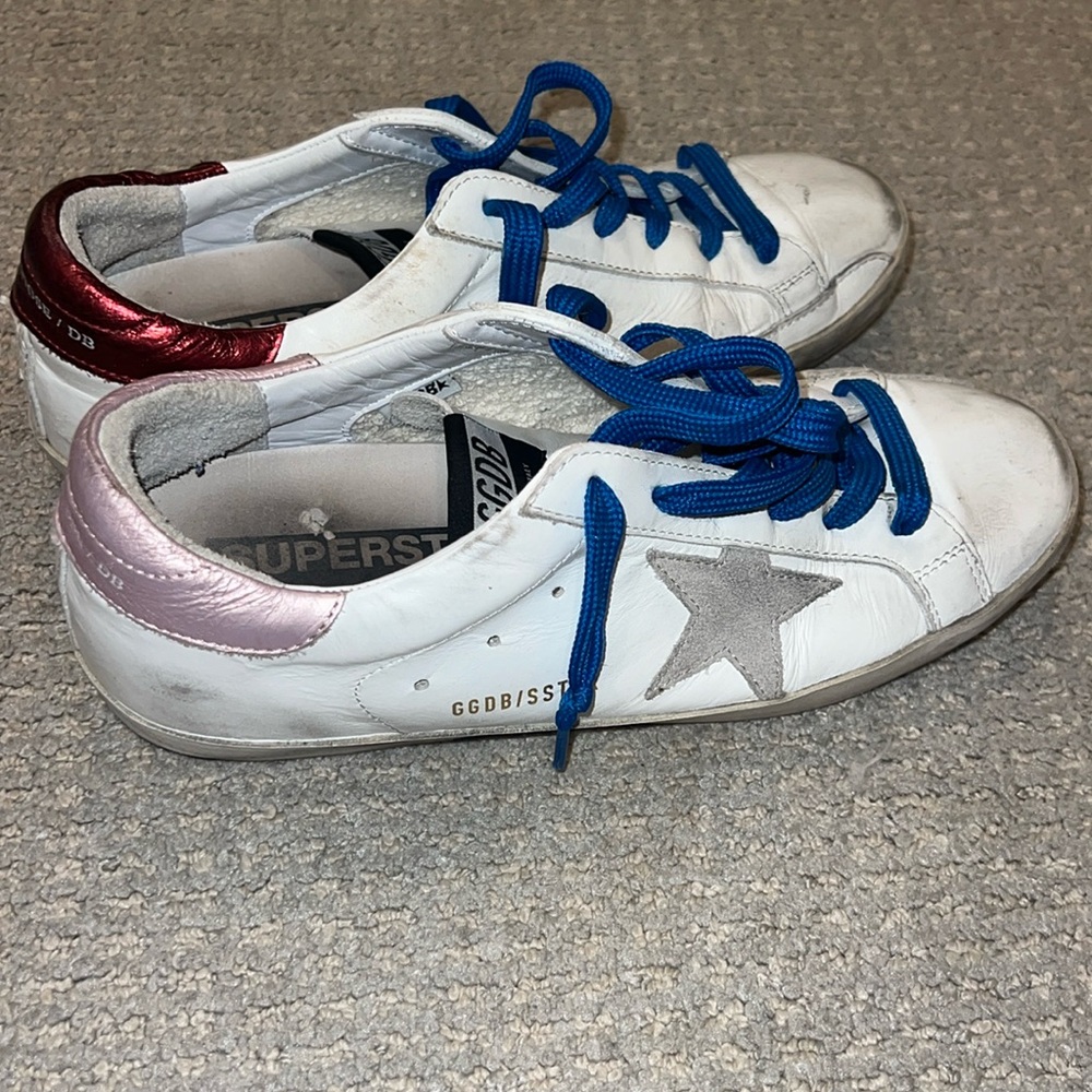 Golden goose star sneakers with red and pink heel tabs and blue laces.